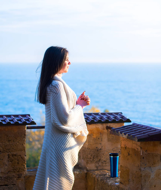 Молодая девушка в белом кардигане любуется утренним видом на море с вершины крепости
 - Фото, изображение