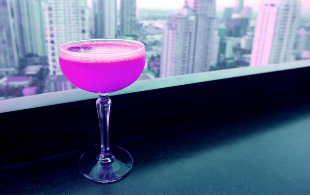 Σοκαριστικό ροζ κοκτέιλ στο τραπέζι του μπαρ της ταράτσας με θέα στους ουρανοξύστες στο φόντο - Φωτογραφία, εικόνα
