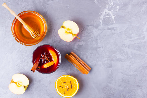 Glass of mulled wine with spices on cement background. Christmas mulled wine with orange, apple, star anise and cinnamon. Red mulled wine and honey on a gray background. Top view. Copy space - Foto, Imagem