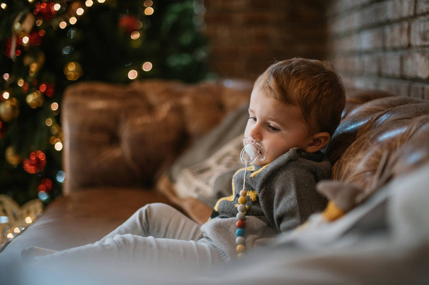 Πορτρέτο ενός μωρού στον καναπέ κοντά στο χριστουγεννιάτικο δέντρο με δώρα - Φωτογραφία, εικόνα