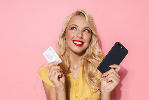 Image of young woman smiling while holding cellphone and credit card - Fotó, kép