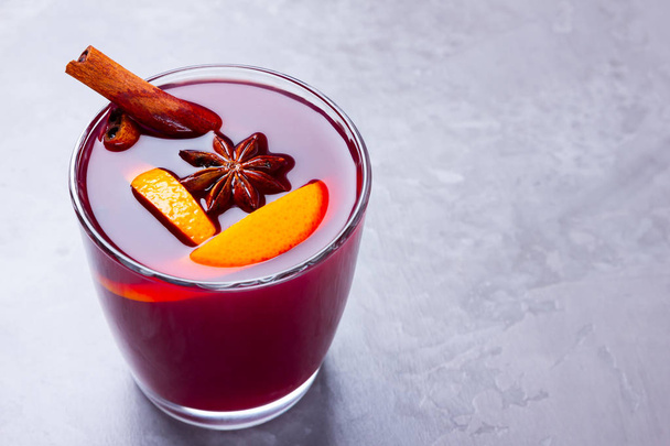 Glass of mulled wine with spices on cement background. Christmas mulled wine with orange, star anise and cinnamon. Red mulled wine on a gray background. Minimalism. Copy space - Valokuva, kuva