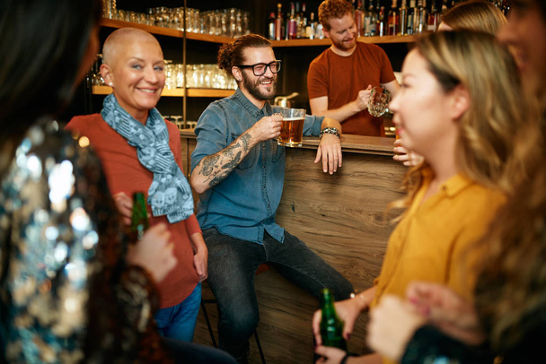 Grupo de amigos bebiendo cerveza, charlando y divirtiéndose en el pub. Noche fuera.
. - Foto, imagen