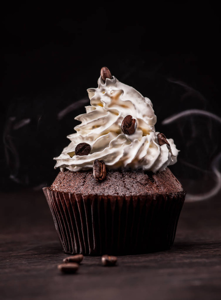 Schokoladenmuffin mit Kaffeebohnen und Sahne auf dunklem Hintergrund mit Dampf  - Foto, Bild