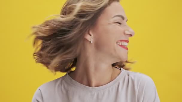 Attractive young woman with red lips laughing and shaking her head with her hair over yellow background isolated - Footage, Video