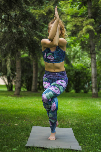 Girl with curly blond hair practices yoga in the park. - 写真・画像