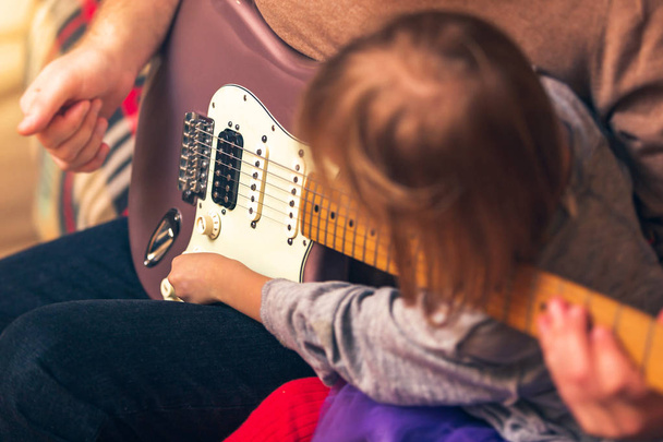 Söpö tyttö ja hänen isänsä soittavat kitaraa ja hymyilevät istuessaan sohvalla kotona. Viettää aikaa yhdessä, oppia soittamaan kitaraa
. - Valokuva, kuva