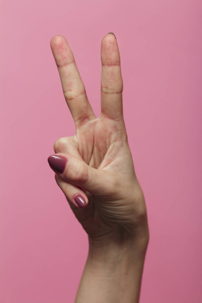 vrouwelijke handen tonen nummer twee als onderdeel van datum van nieuwjaar 2020, gebarentaal op een gekleurde roze achtergrond - Foto, afbeelding