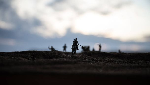 Ο παγκόσμιος αξιωματικός του πολέμου (ή πολεμιστής) αναβάτης στο άλογο με ένα σπαθί έτοιμο να πολεμήσει και στρατιώτες σε ένα σκοτεινό φόντο με θολή απόχρωση. Μάχη σκηνή μάχης των στρατιωτών της μάχης. - Φωτογραφία, εικόνα