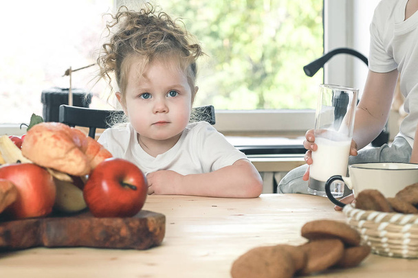 Portret van schattig klein meisje met gehaakte speelgoed zitten aan tafel in lichte keuken wachten op ontbijt. - Foto, afbeelding
