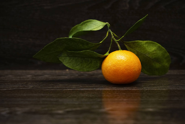 Fresh, ripe tangerine  with leaves on a black stone surface. - Foto, afbeelding