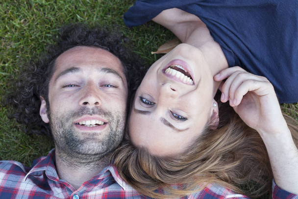 Over head close up portrait of a young and attractive couple laying down on grass. Love and relationship concept - Fotó, kép