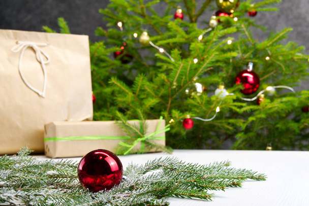 Hermosa composición navideña. Cajas de regalo y árbol de Navidad con luces en el fondo. Decoración bola roja con rama de abeto. Fondo de Navidad para su tarjeta de felicitación con espacio para el texto
. - Foto, Imagen