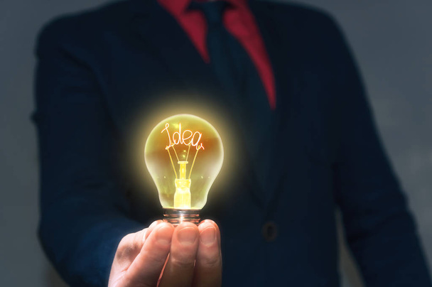 De zakenman houdt een lamp met een nieuw idee voor je. Concept van een nieuw idee, nieuwe ontdekking. - Foto, afbeelding