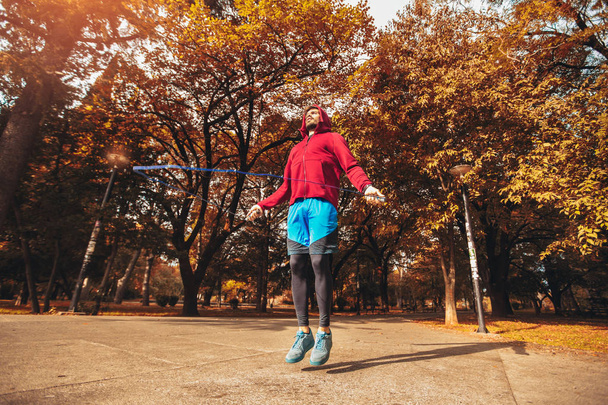 Man jumping rope outdoors on sunny autumn morning. - 写真・画像