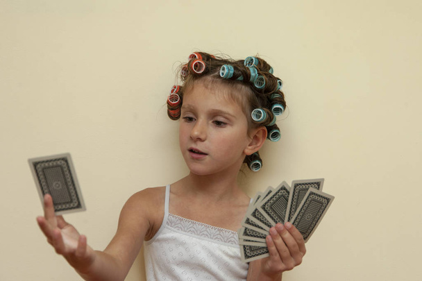 The little girl in hair rollers with game cards. - Photo, Image