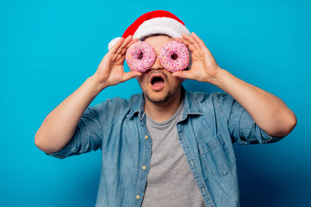 Knappe man in kerstmuts met donuts op blauwe achtergrond - Foto, afbeelding