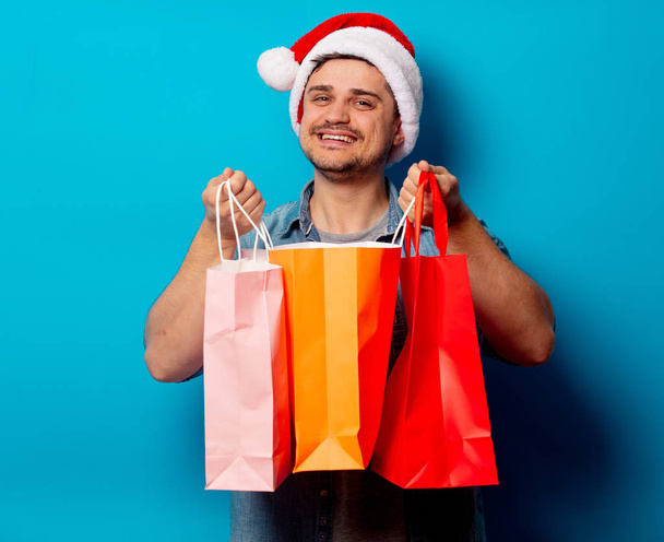 Hombre guapo en sombrero de Navidad con bolsas de compras en fondo azul
 - Foto, imagen