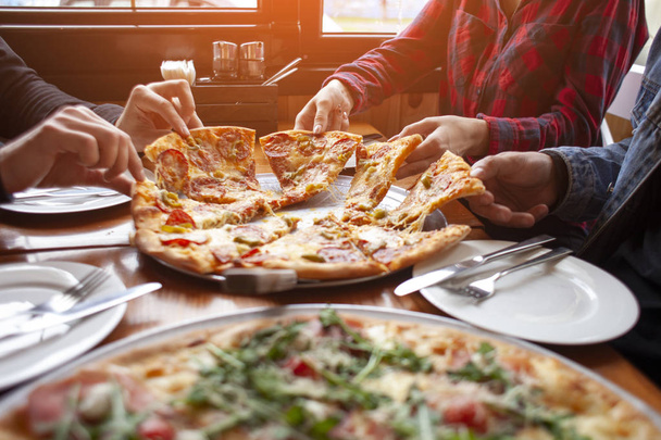 grupo de estudiantes amigos comen pizza italiana, las manos toman rebanadas de pizza en un restaurante
 - Foto, Imagen