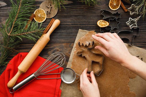 Mujer preparando sabrosas galletas de Navidad en forma de ciervo en la mesa. Asiento plano, vista superior. Ambiente navideño
 - Foto, imagen