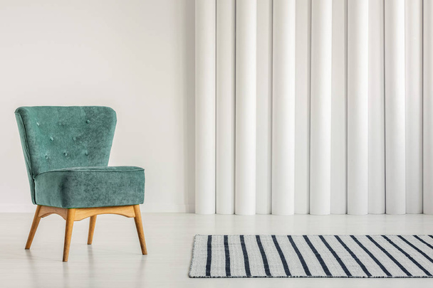 Stylish turquoise armchair in empty white interior with striped rug - Foto, afbeelding