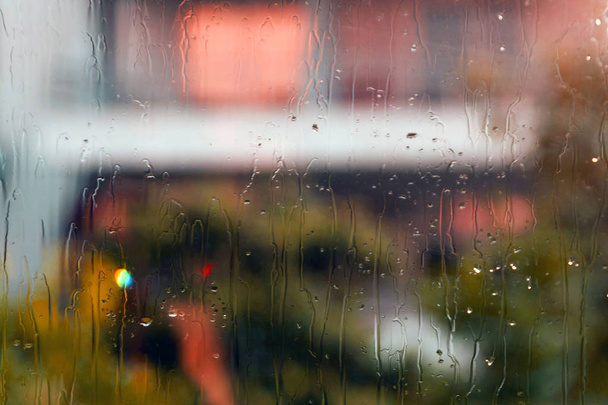nasses Fensterglas mit Regentropfen und bunten abstrakten Unschärfen und Silhouetten auf der Straße - Foto, Bild