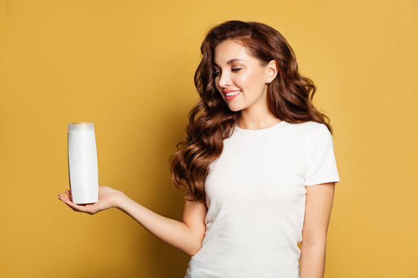 Pretty woman looking at white cosmetic tube in her hand on yellow - Foto, Bild