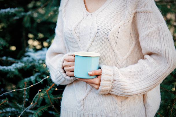 Girl in white sweater holding a cup with coffee near fir tree on - Photo, Image