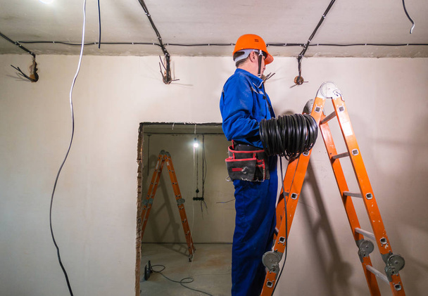 Electrician in hard hat and uniform holding a cable roll in his hands - Zdjęcie, obraz