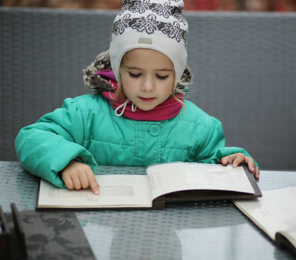 Niña de tres años leyendo un menú en la terraza de la cafetería al aire libre
 - Foto, Imagen