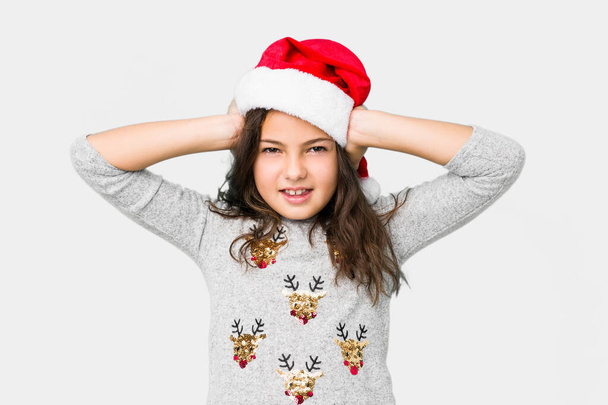 Pikkutyttö juhlii joulua päivä peittää korvat käsillään yrittää olla kuulematta liian kovaa ääntä
. - Valokuva, kuva