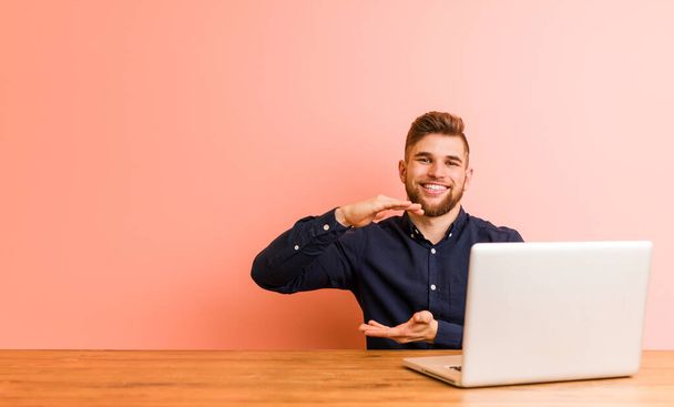 Молодий чоловік працює зі своїм ноутбуком, тримаючи щось обома руками, презентація продукту
. - Фото, зображення