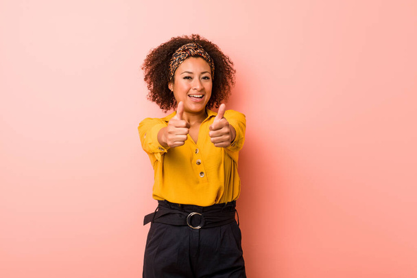Young african american woman against a pink background with thumbs ups, cheers about something, support and respect concept. - Valokuva, kuva