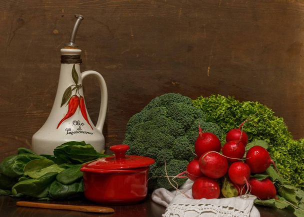 stilleven met broccoli, sla, spinazie, radijs, een kleine rode steelpan en een kan olijfolie op een linnen doek - Foto, afbeelding