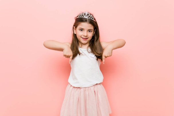 kleines Mädchen mit Prinzessinnen-Look zeigt mit Fingern nach unten, positives Gefühl. - Foto, Bild