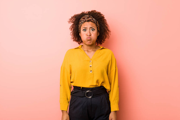 Jeune femme afro-américaine sur un fond rose souffle joues, a l'expression fatiguée. Concept d'expression faciale
. - Photo, image