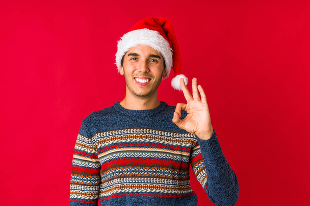 Νεαρός άντρας την ημέρα των Χριστουγέννων κάνει κλίμακα με τα χέρια, αισθάνεται χαρούμενος και σίγουρος. - Φωτογραφία, εικόνα