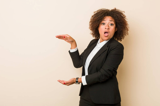 Młody biznes Afrykańska amerykańska kobieta zszokowana i zdumiona trzymając kopię przestrzeni między rękami. - Zdjęcie, obraz