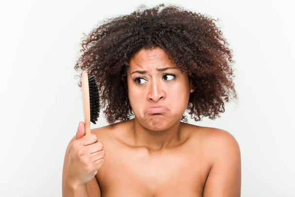 Молодая африканская американка пытается расчесать свои кудрявые волосы
 - Фото, изображение