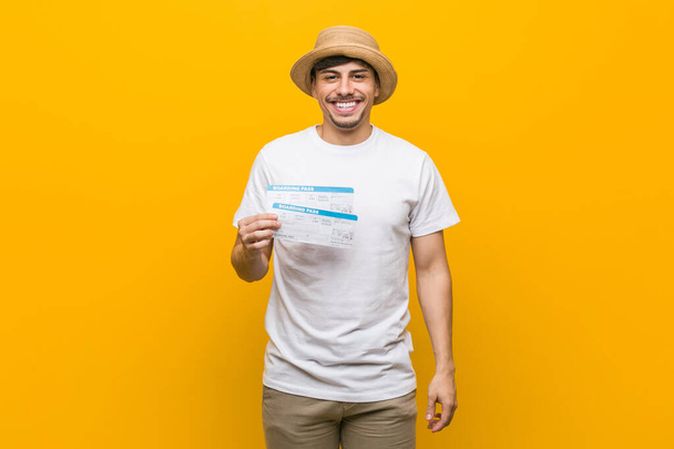 Joven hispano sosteniendo un billete de avión feliz, sonriente y alegre
. - Foto, Imagen