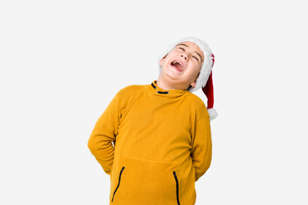 Niño pequeño celebrando el día de Navidad con un sombrero de santa aislado relajado y feliz riendo, cuello estirado mostrando los dientes
. - Foto, Imagen