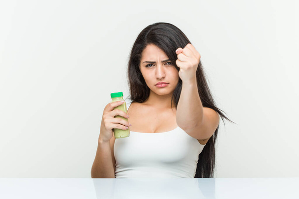 Fiatal spanyol nő kezében egy növényi ital mutatja ököllel a kamera, agresszív arckifejezés. - Fotó, kép