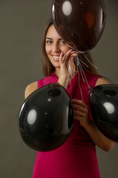 Приваблива жінка в сукні фуксії, що тримає чорні кульки, концепція вечірки та святковий сезон
 - Фото, зображення