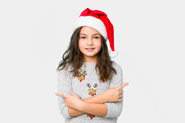 Klein meisje vieren kerstdag punten zijwaarts, probeert te kiezen tussen twee opties. - Foto, afbeelding