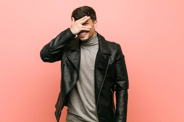 Young hispanic man wearing a leather jacket blink at the camera through fingers, embarrassed covering face. - Fotoğraf, Görsel