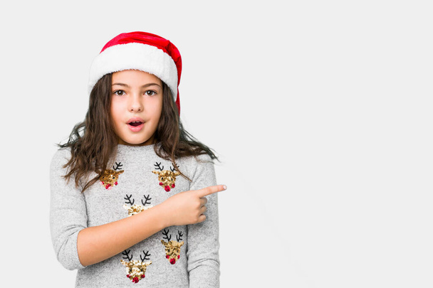 Little girl celebrating christmas day pointing to the side - Fotografie, Obrázek
