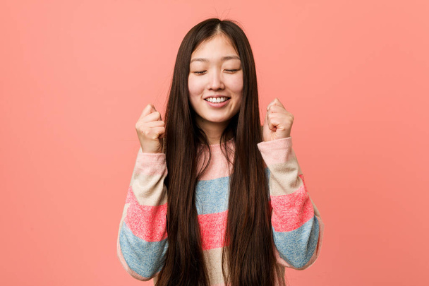 Молодая крутая китаянка поднимает кулак, чувствует себя счастливой и успешной. Идея победы
. - Фото, изображение