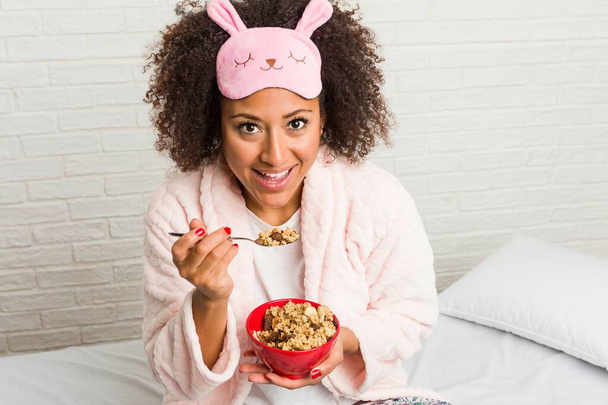 Joven mujer afroamericana comiendo un tazón de cereal en la cama
 - Foto, imagen