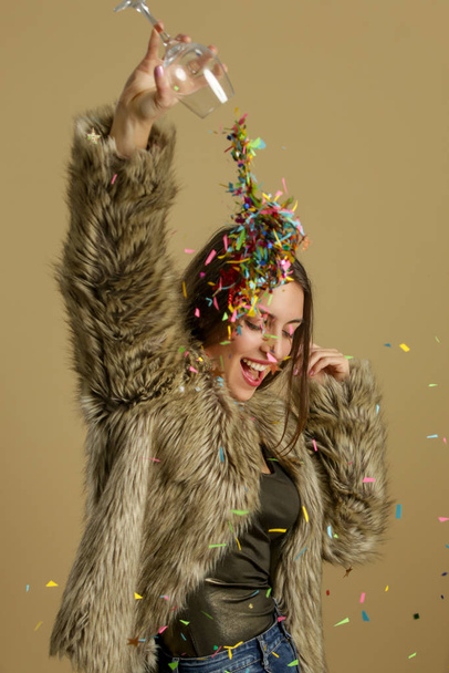 Elegant happy woman in fur coat holding a glass full of colorful confetti, party, holiday and celebration concept - Foto, imagen