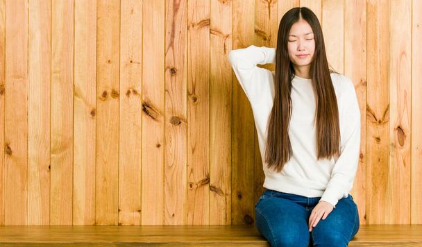 Jeune femme chinoise assise sur un endroit en bois souffrant de douleurs au cou dues à un mode de vie sédentaire
. - Photo, image